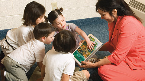 mujer mostrándole a cuatro niños una ilustración que representa la naturaleza