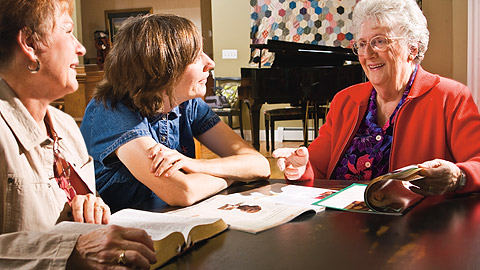 três mulheres sentadas junto a uma mesa, estudando o evangelho juntas
